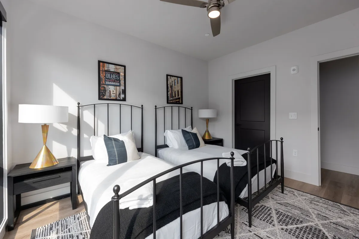A bedroom with two twin beds, decorative lamps, and expressive artwork on the walls. The space feels comfortable and bright, suitable for friends, family, or colleagues seeking flexibility in sleeping arrangements.