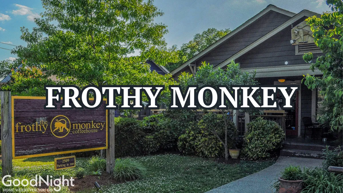 The exterior of the Frothy Monkey coffeehouse, with warm wooden architecture, lush landscaping, and guests enjoying coffee outdoors. The setting is lively and welcoming, inviting both socializing and remote work.