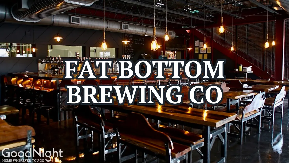 A vibrant bar and dining space with long wooden tables, industrial light fixtures, a visible bar area, and staircase. People are socializing and the ambiance hints at live music nights and craft beer tastings.