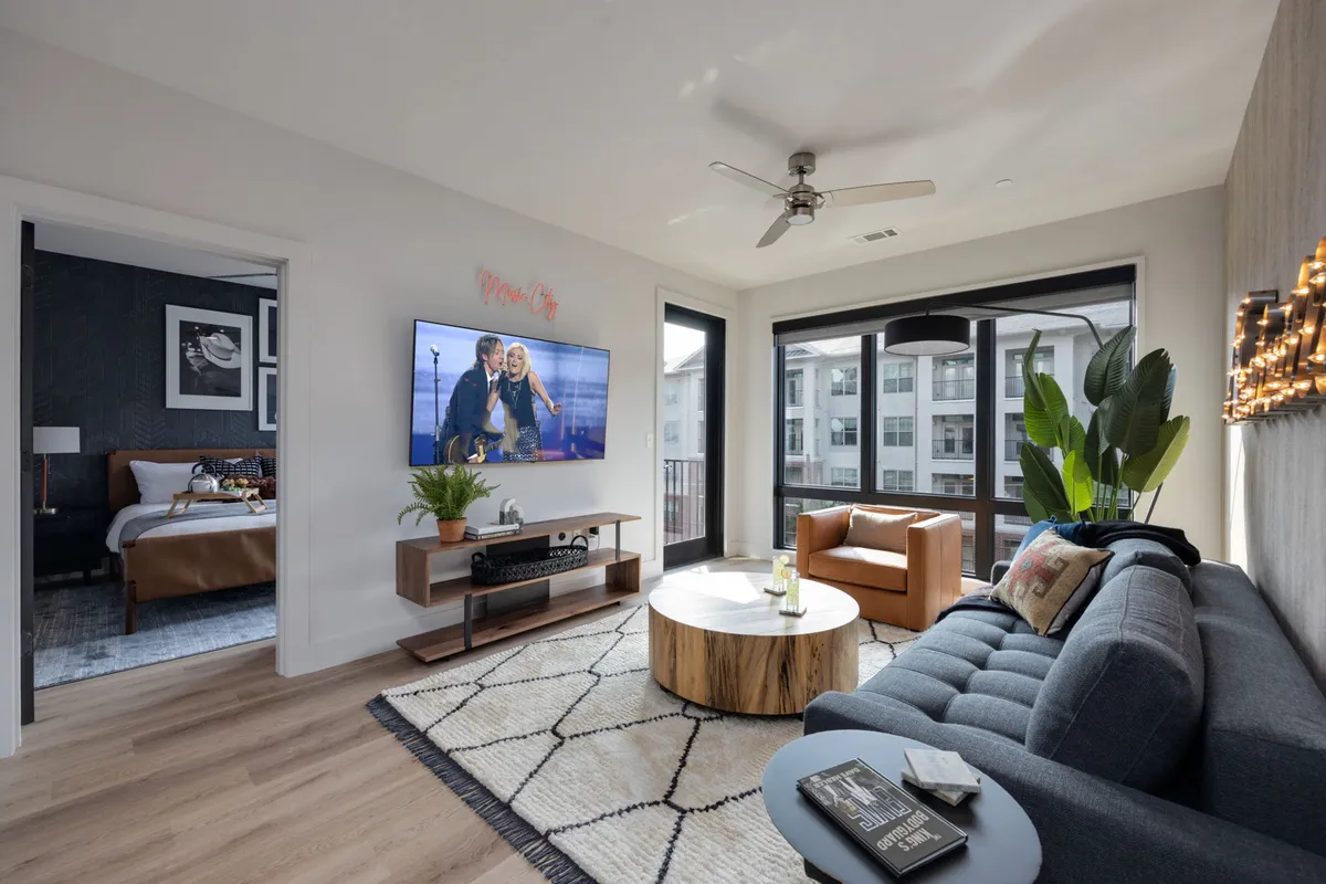 The image showcases a stylish, inviting living space with a plush sofa, modern coffee table, large TV, lush houseplant, and striking artwork. The setup radiates comfort and is perfect for gathering with friends or unwinding after a day exploring Nashville.