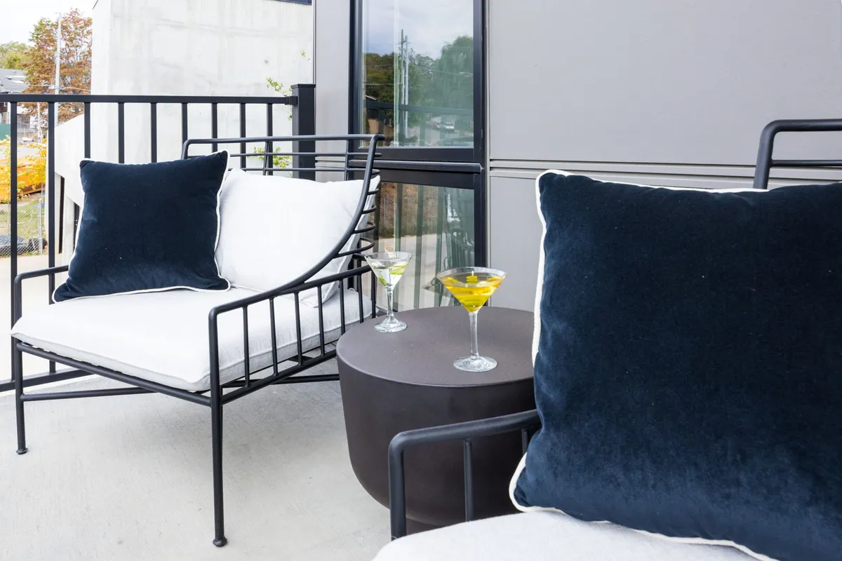 An elegant outdoor patio scene with two black and white chairs, a small round table, and two cocktails, all set against a backdrop hinting at urban views. The setup is designed for relaxation, casual conversation, and enjoying the outdoors—ideal for unwinding after a day exploring local attractions.