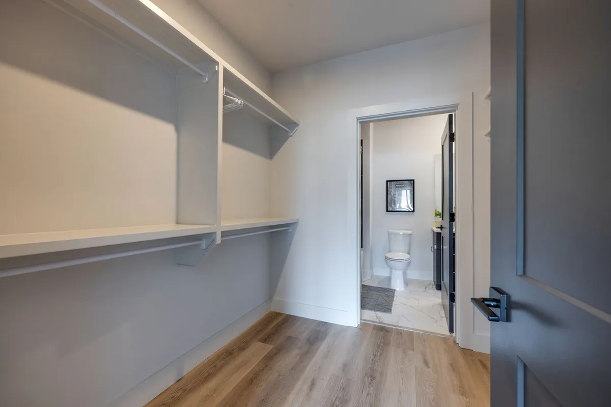 A calm, functional closet space with shelving and a doorway leading to the bathroom. Light wood flooring and simple storage solutions offer guests plenty of space to organize personal belongings during their stay.
