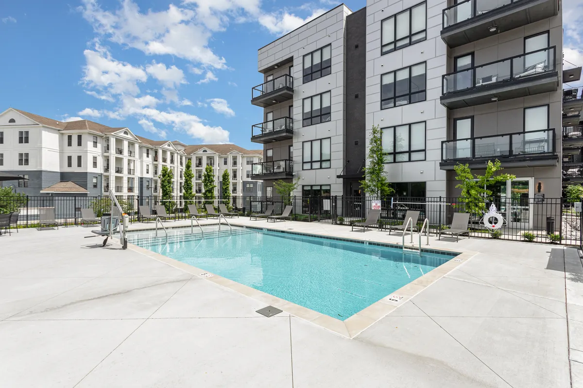 This image features the resort-style swimming pool surrounded by lush greenery and modern balconies, capturing the relaxed and social atmosphere central to the complex's amenities. Lounge chairs line the pool, suggesting spaces for both sunbathing and social gatherings.